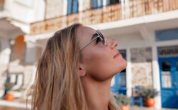 A girl in sunglasses looking up to the sky in front of a blue and white building