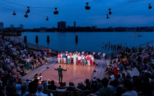 An outdoor stage performance for a large group of people riverside.