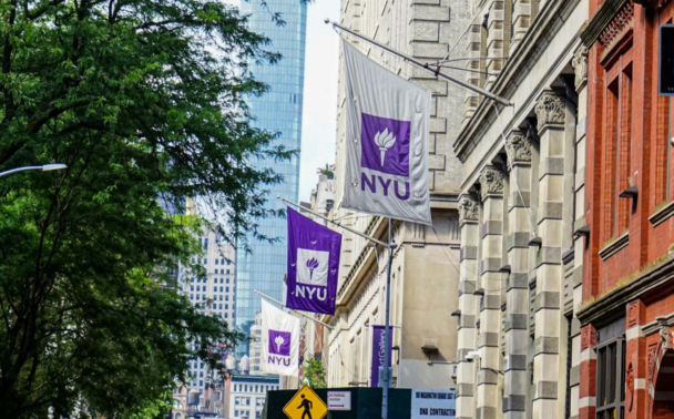 Image of a New York City street with hanging flags with "NYU" on them.